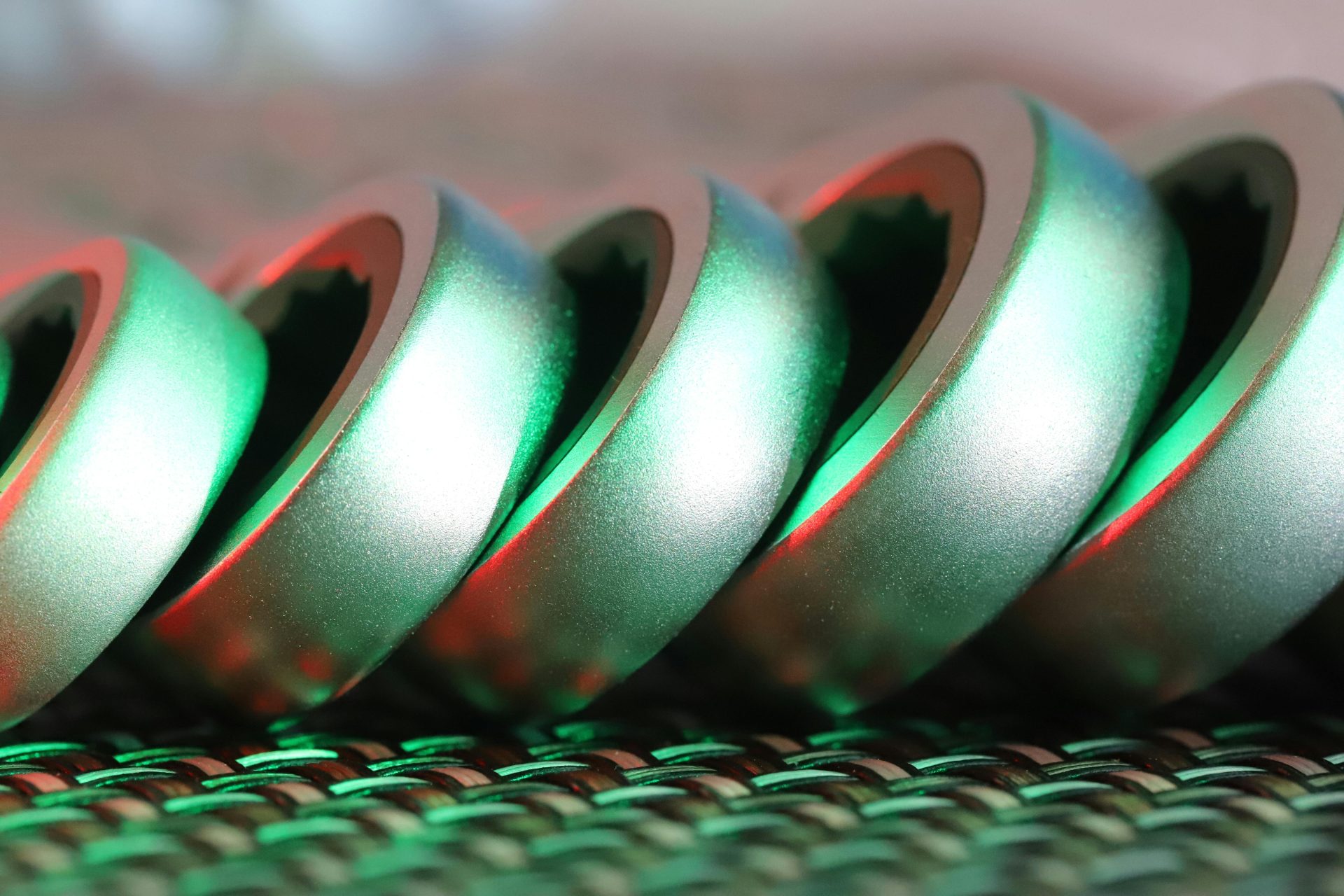 Fotografía macro de una espiral metálica con vibrantes reflejos de luz verde y roja, que resaltan la textura y la forma.